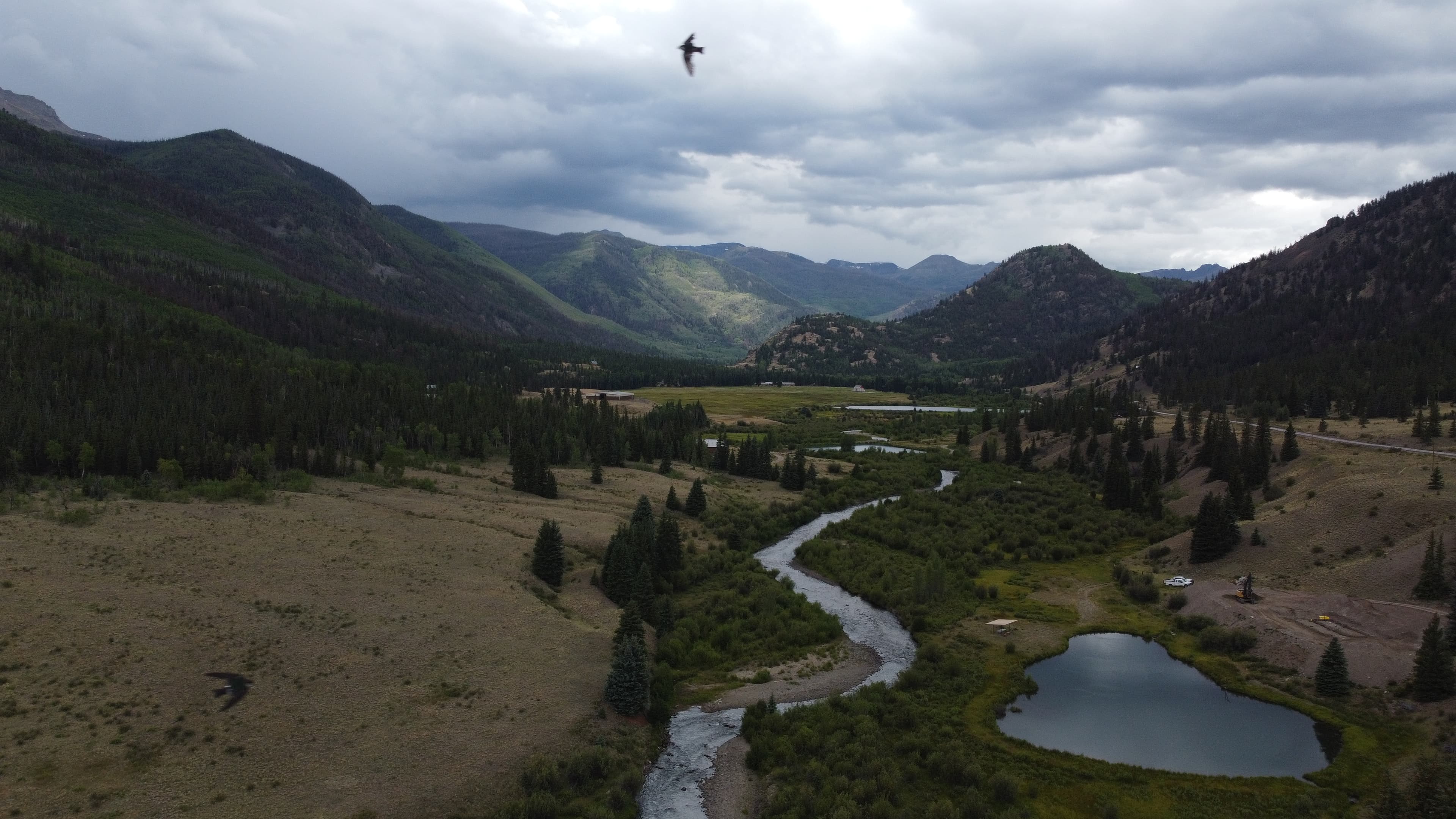 Wide drone view of mountain valley with pond and winding river