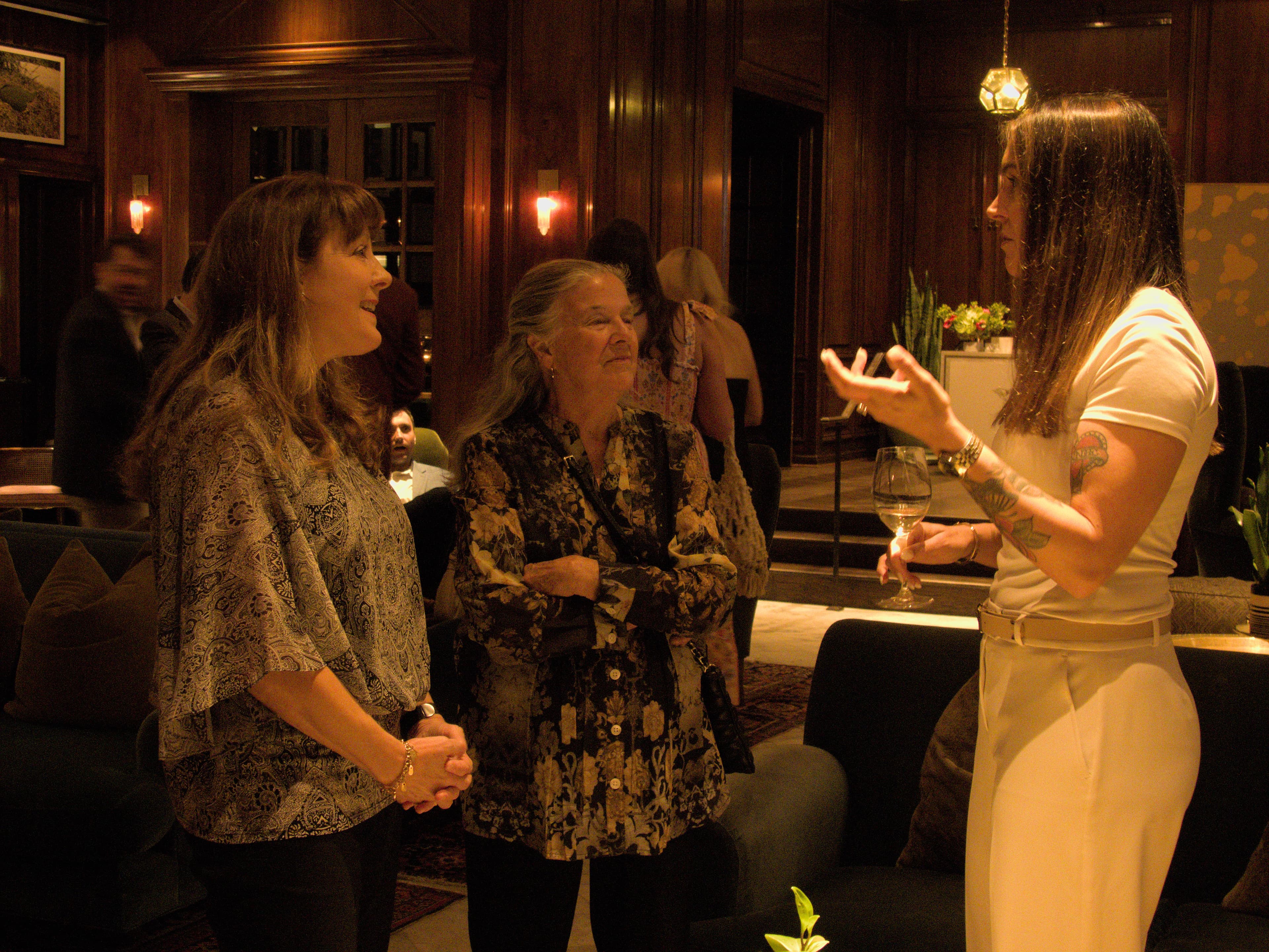 Three women in candid conversation at evening event