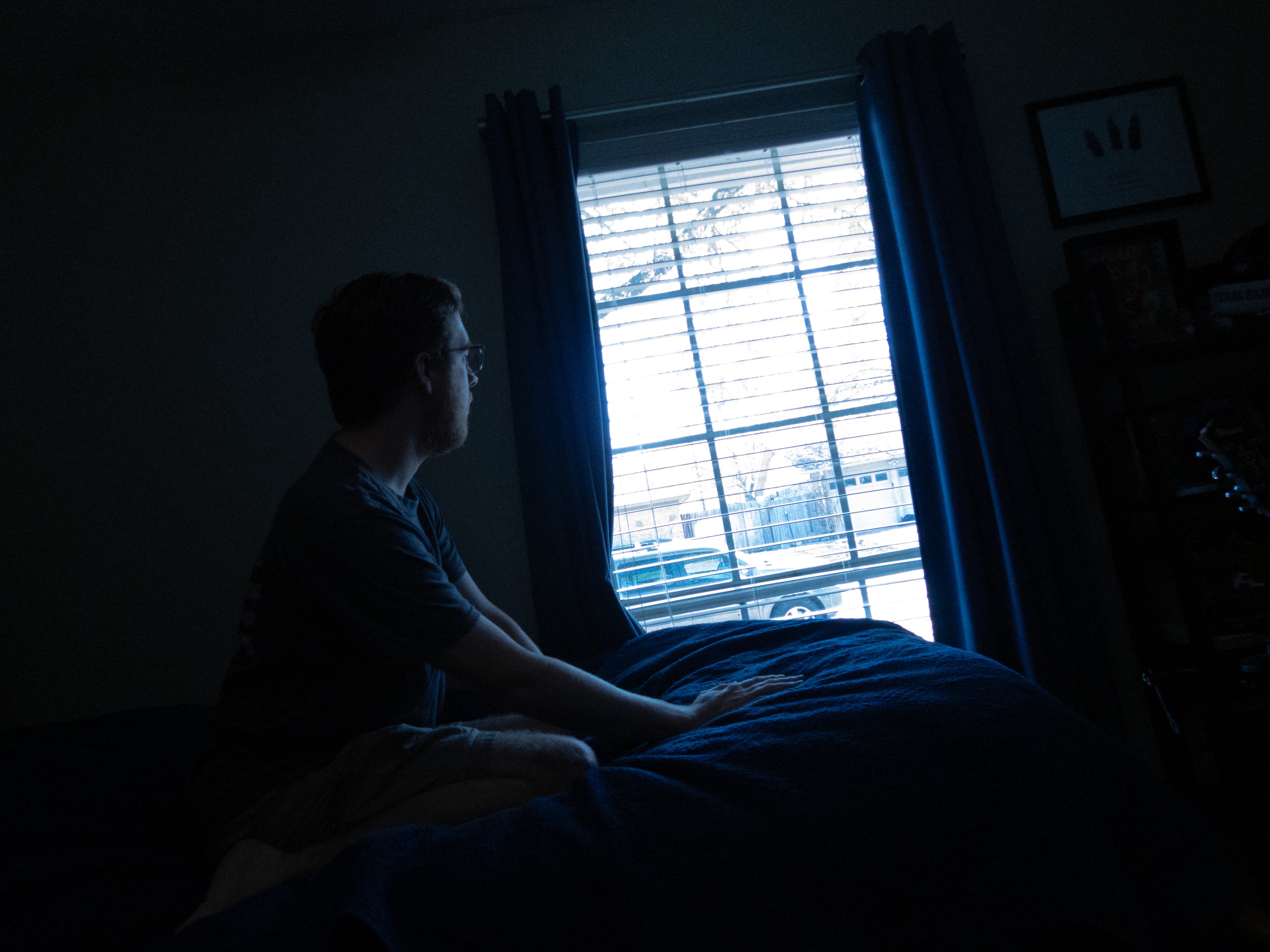 Sitting on the edge of the bed, watching the morning through the blinds